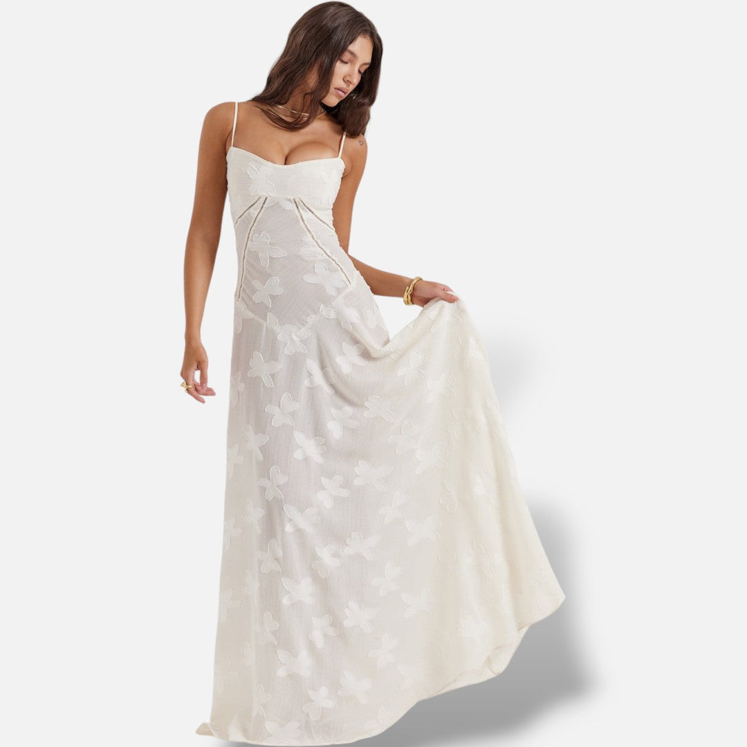 Modelo veste vestido maxi branco El Armario de Lola com alças finas, corte justo e padrão floral subtil em tecido sedoso